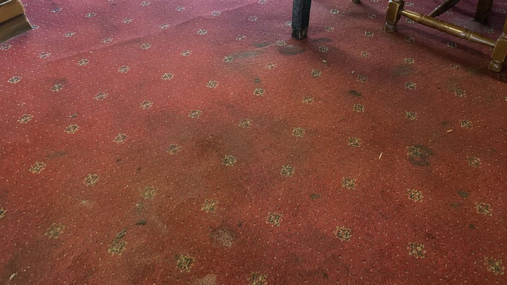 A very dirty, soiled red pub carpet.